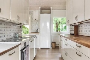 A kitchen with white cabinets, a wooden countertop, and a window with a view of greenery. - Swedish archipelago retreat with sauna in Bökevik (Ronneby)