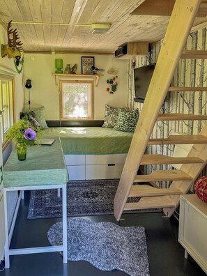 A cozy room with a bed, a desk, a window, a staircase, and a wall with a tree pattern. - Small cabin with outdoor kitchen by forest stream (Trollhättan)