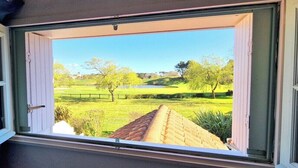 Una ventana con vista a un campo verde, árboles y un edificio en la distancia.