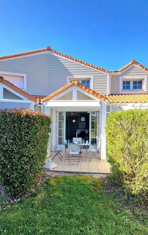 A two-story house with a patio area, a kitchen visible through the glass door, and a well-maintained lawn. - Violette, a pretty house in the heart of the golf (Talmont-Saint-Hilaire)