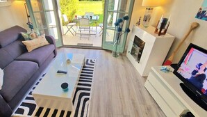 Una sala de estar con sofá, mesa de centro, televisor y puerta de vidrio que da a un espacio exterior.