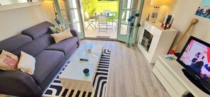 A living room with a sofa, coffee table, TV, and a glass door leading to an outdoor area. - Violette, a pretty house in the heart of the golf (Talmont-Saint-Hilaire)