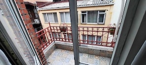 A balcony with a red metal railing, a tiled floor, and a building with multiple windows in the background. - Puffin Hostel (Istanbul)