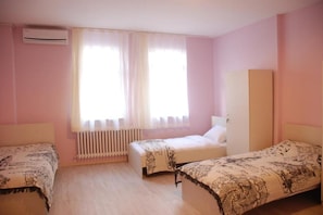 Quarto com duas camas, radiador, ar condicionado e janela com cortinas leves.