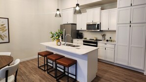 A modern kitchen with white cabinetry, a central island with stools, and pendant lighting. - Relax & Recharge in Perham's Lakes Country ~ Family-friendly 3BR Retreat (Perham)