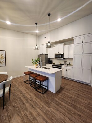 A modern kitchen with white cabinetry, a central island with stools, and pendant lighting.