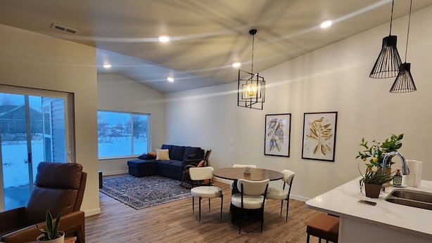A modern kitchen with a dining area, wooden flooring, pendant lighting, and artwork on the walls. - Relax & Recharge in Perham's Lakes Country ~ Family-friendly 3BR Retreat (Perham)
