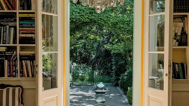 An open door leading to a garden with a fountain, a chandelier, and a table with a bowl of fruits. - Charming artist's house in Söderåkra (Söderåkra)
