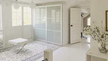 A spacious room with a large sliding door, a bed with a white headboard, a patterned rug, and a vase with flowers on a side table.