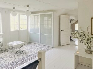 A spacious room with a large sliding door, a bed with a white headboard, a patterned rug, and a vase with flowers on a side table. - Charming artist's house in Söderåkra (Söderåkra)