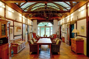 A dining area with a long table and wicker chairs, a chandelier, and a high ceiling with wooden beams. - Historic farmhouse near the Schaalsee lake (Vellahn OT Camin)