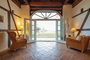 A room with a large arched doorway, wicker furniture, and a tiled floor. - Historic farmhouse near the Schaalsee lake (Vellahn OT Camin)