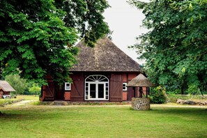 A rustic building with a thatched roof, a large arched doorway, and a stone structure in front. - Historic farmhouse near the Schaalsee lake (Vellahn OT Camin)