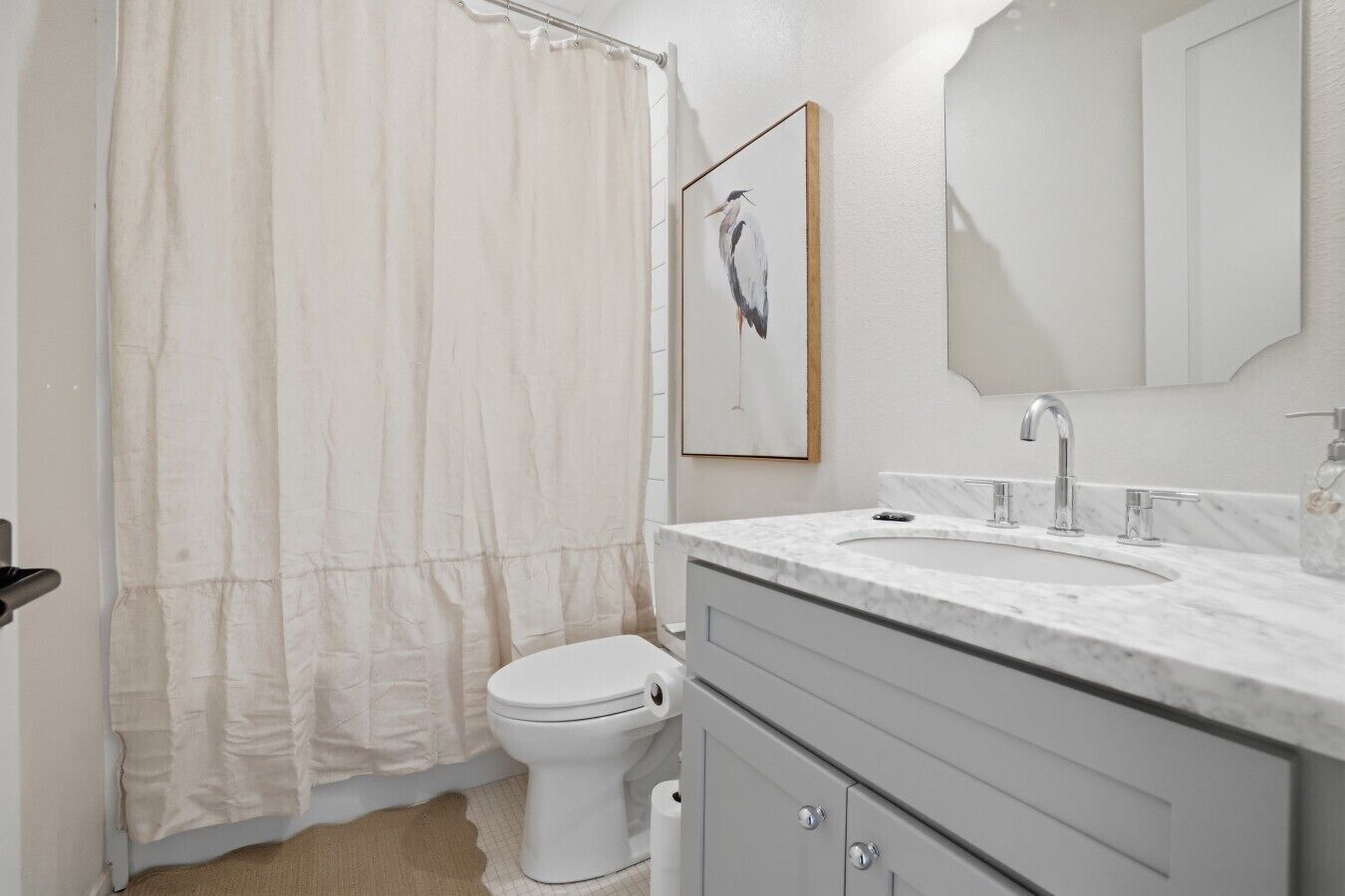 A bathroom with a toilet, a sink with a marble countertop, a shower curtain, and a framed picture on the wall.