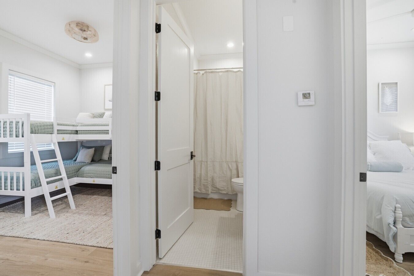 Een slaapkamer met stapelbedden, een badkamer met douchegordijn en een witte deur.