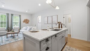 Una cocina moderna con una isla central, un comedor con sofá y una sala de estar con mesa de centro.