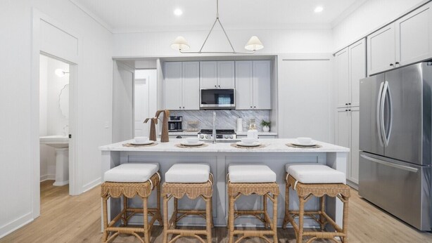 Una cocina moderna con armarios blancos, un refrigerador de acero inoxidable, una isla central con taburetes y luminarias colgantes.