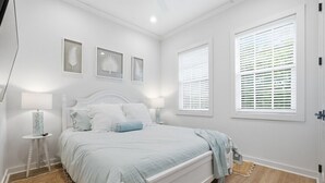 Un dormitorio con cama, lámparas de noche, alfombra y ventana con persianas.