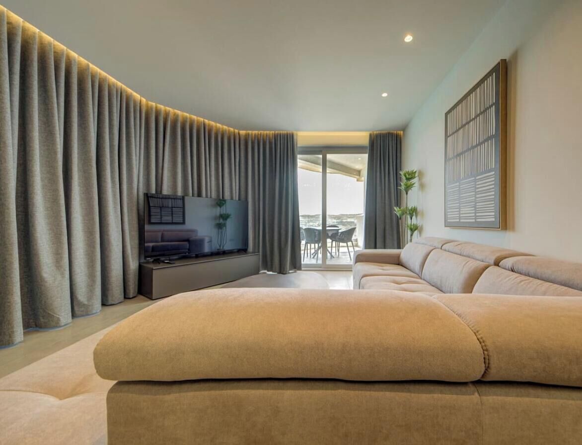 Een moderne woonkamer met een grote bank, een flatscreen-televisie en een balkon met een tafel en stoelen.