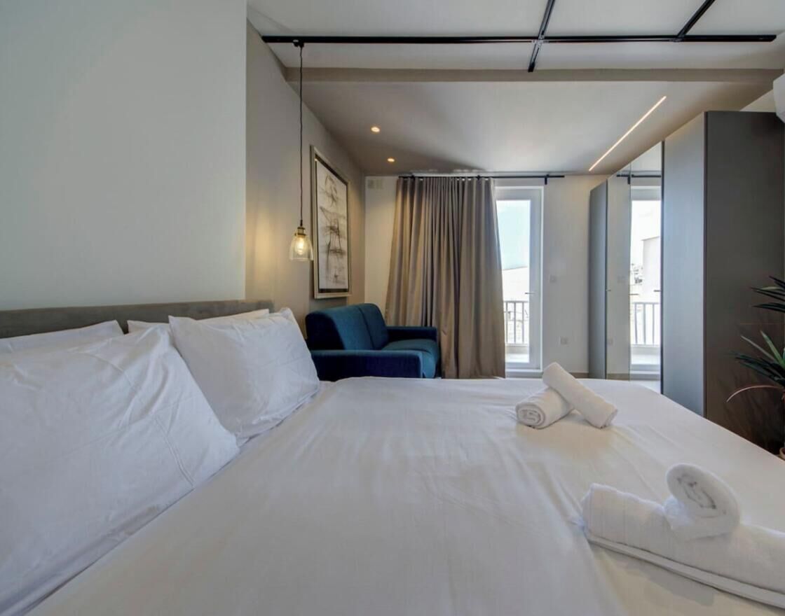 Een hotelkamer met een groot bed, een stoel, een raam met gordijnen en een balkon.