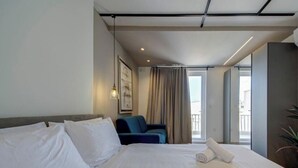 Quarto de hotel com uma cama grande, uma cadeira, uma janela com cortinas e uma varanda.