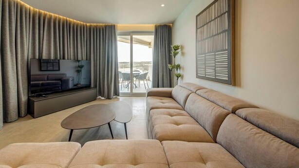Uma sala de estar moderna com sofá, televisão, mesa pequena e varanda com vista.