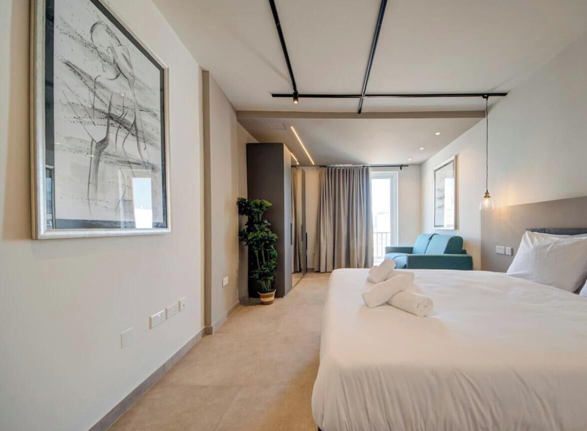 Een moderne hotelkamer met een groot bed, een kamerplant, uitzicht over de stad en een groot abstract schilderij aan de muur.