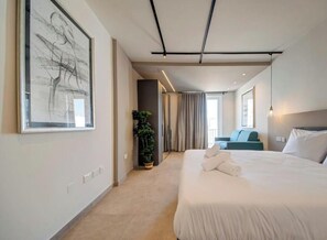 Ein modernes Hotelzimmer mit einem großen Bett, einer Zimmerpflanze, Blick auf die Stadt und einem großen abstrakten Gemälde an der Wand.