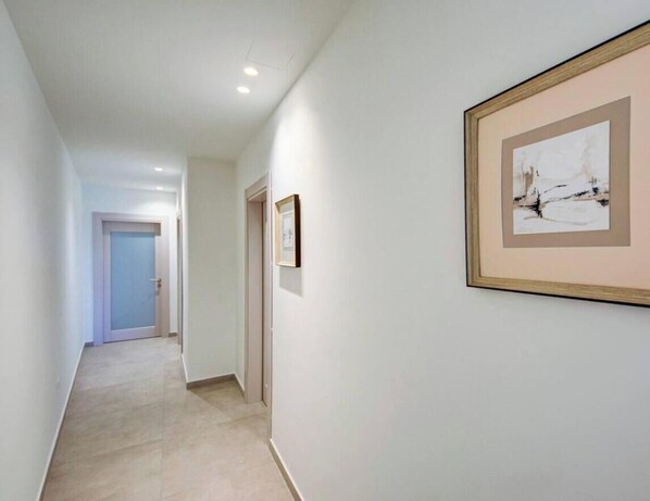 Un pasillo con un cuadro enmarcado en la pared, una puerta al final y una lámpara en el techo.