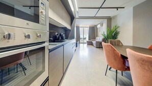 Eine moderne Küche mit Einbauofen, ein Essbereich mit Tisch und Stühlen sowie eine Couch im Hintergrund.