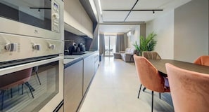 Eine moderne Küche mit Einbauofen, ein Essbereich mit Tisch und Stühlen sowie eine Couch im Hintergrund.