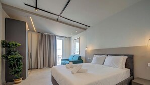Ein modernes Hotelzimmer mit einem großen Bett, einer Zimmerpflanze, einer Couch und Blick ins Freie.