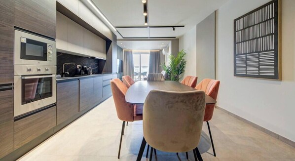 Una cocina moderna con electrodomésticos integrados, un comedor con una mesa grande y sillas, y vistas al exterior.
