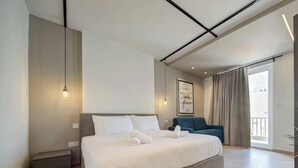 Ein modernes Hotelzimmer mit einem großen Bett, einem Nachttisch, einem Sessel und einem Balkon mit Vorhängen.