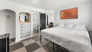 Un dormitorio con cama, cómoda, espejo, puerta y un cuadro en la pared.