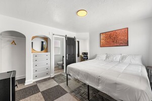 Un dormitorio con cama, cómoda, espejo, puerta y un cuadro en la pared.