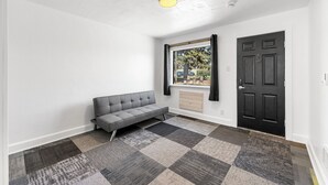 Una habitación con un sofá gris, un suelo de alfombra a cuadros, una puerta negra y una ventana con cortinas.