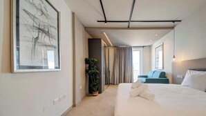 Moderni hotellihuone, jossa on suuri sänky, ruukkukasvi ja näkymä käytävään.