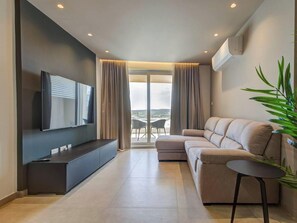 Ein modernes Wohnzimmer mit Flachbildfernseher, einer Couch, einem Couchtisch und einer Pflanze.