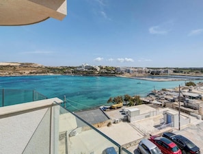 Blick auf die Küste mit blauem Meer, Gebäuden im Hintergrund und geparkten Autos.