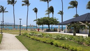 A pathway leading to a beachside area with palm trees, a covered seating area, and a view of the ocean.
