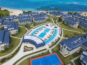 Un resort con varias edificaciones, un área de piscina central y una playa.