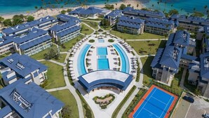 A resort with multiple buildings, a central pool, and a beach view.