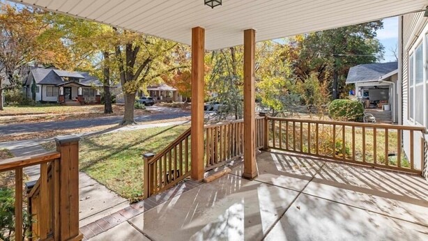 A covered porch with a wooden railing, a lantern, and a view of a residential street with houses and trees. - Quiet College Hill Getaway—Two Kings, Two Queens, remodeled kitchen and Bath (Wichita)