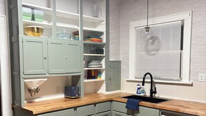 A kitchen with grey cabinets, a wooden countertop, a stainless steel dishwasher, and a window with a hanging light. - Quiet College Hill Getaway—Two Kings, Two Queens, remodeled kitchen and Bath (Wichita)