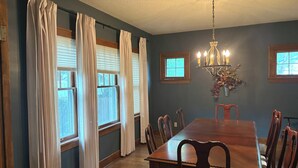 A dining room with a wooden table and chairs, a chandelier, and windows with curtains. - Quiet College Hill Getaway—Two Kings, Two Queens, remodeled kitchen and Bath (Wichita)