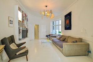 A living room with a sofa, armchair, bookshelf, and a television. - Historic apartment in the heart of Østerbro (København)