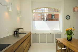 A modern kitchen with a large window, wooden cabinets, a sink, and a dining area with a table and chairs. - Historic apartment in the heart of Østerbro (København)