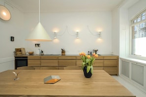 A modern kitchen with wooden cabinets, a dining table, and a vase with flowers. - Historic apartment in the heart of Østerbro (København)