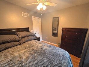 A bedroom with a bed, a dresser, a ceiling fan, and a door. - KC Strong: Beautiful 2 BR Home, Close to stadiums and downtown. (Independence)